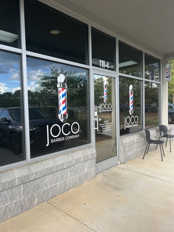 The Bratton Drive storefront on a clear afternoon, barber poles painted on the glass.